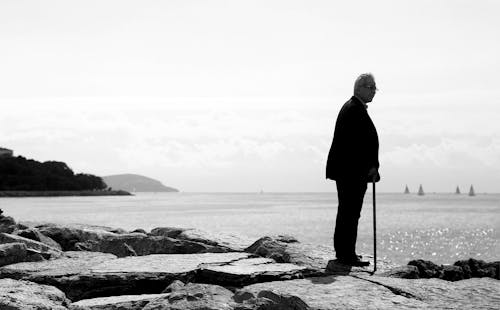 Black and White Photo of Man Standing on Sea Coastline