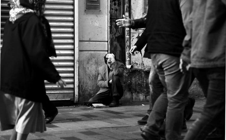 A Man In Blazer Squatting On The Street Near The Shutter