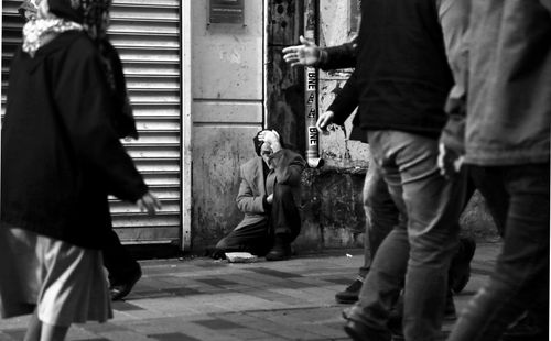 Free Black and white photo of an elderly man in distress, surrounded by pedestrians on a city street. Stock Photo