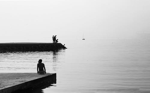 Person Sitting on Concrete Dock in Grayscale Photography