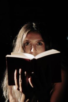 A woman reads a book by night, her face illuminated in a mysterious setting.