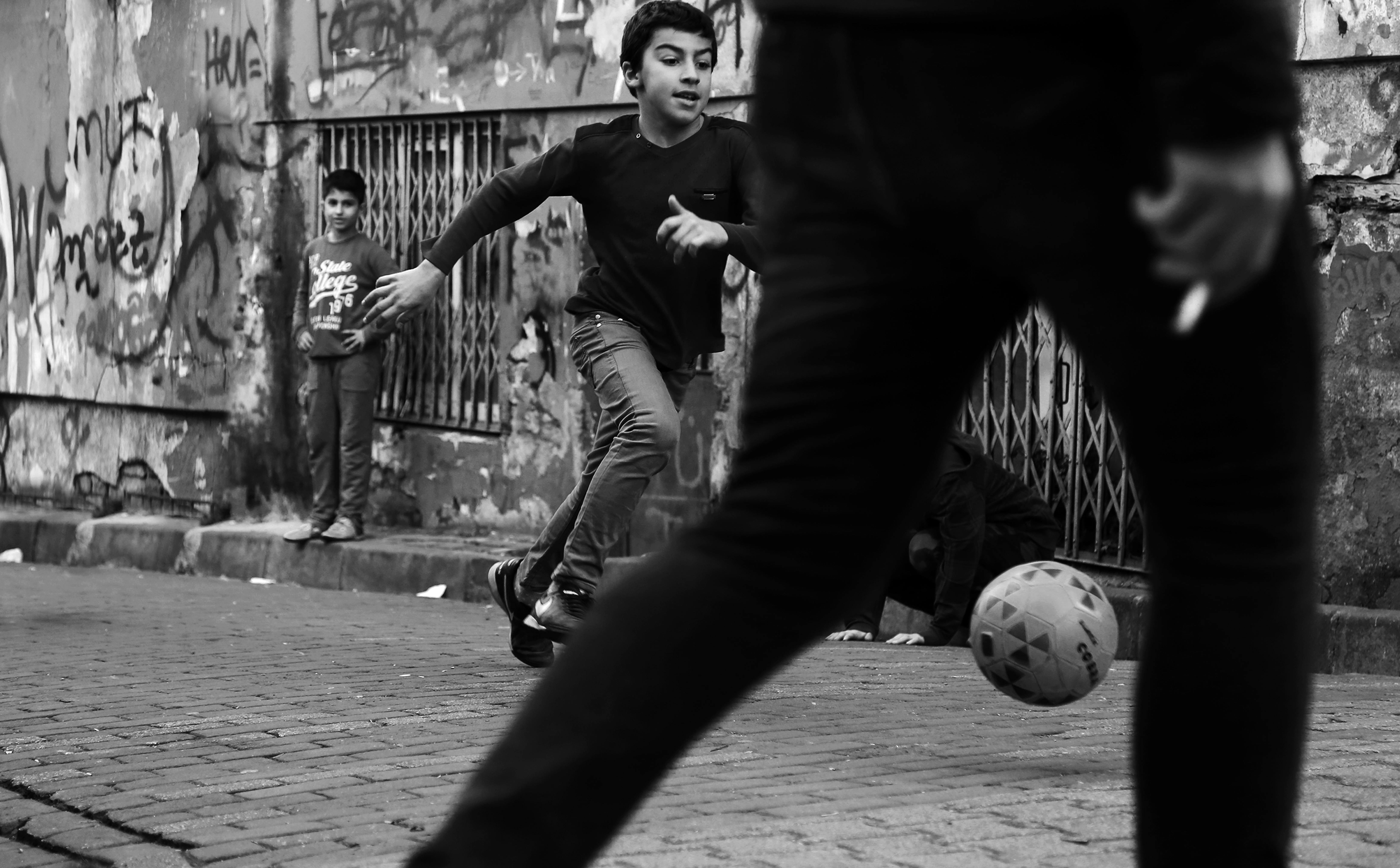 Black and white photo of children playing street soccer in an urban setting.