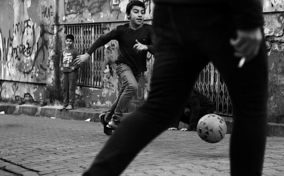Black and white photo of children playing street soccer in an urban setting.
