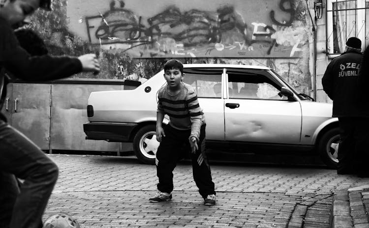 A Boy Playing Soccer Near The Packed Car