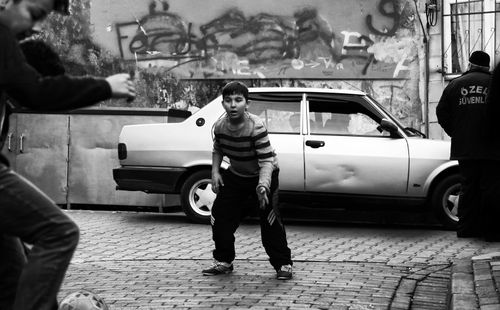 Free Black and white photo of kids playing soccer on a brick street with a parked car. Stock Photo