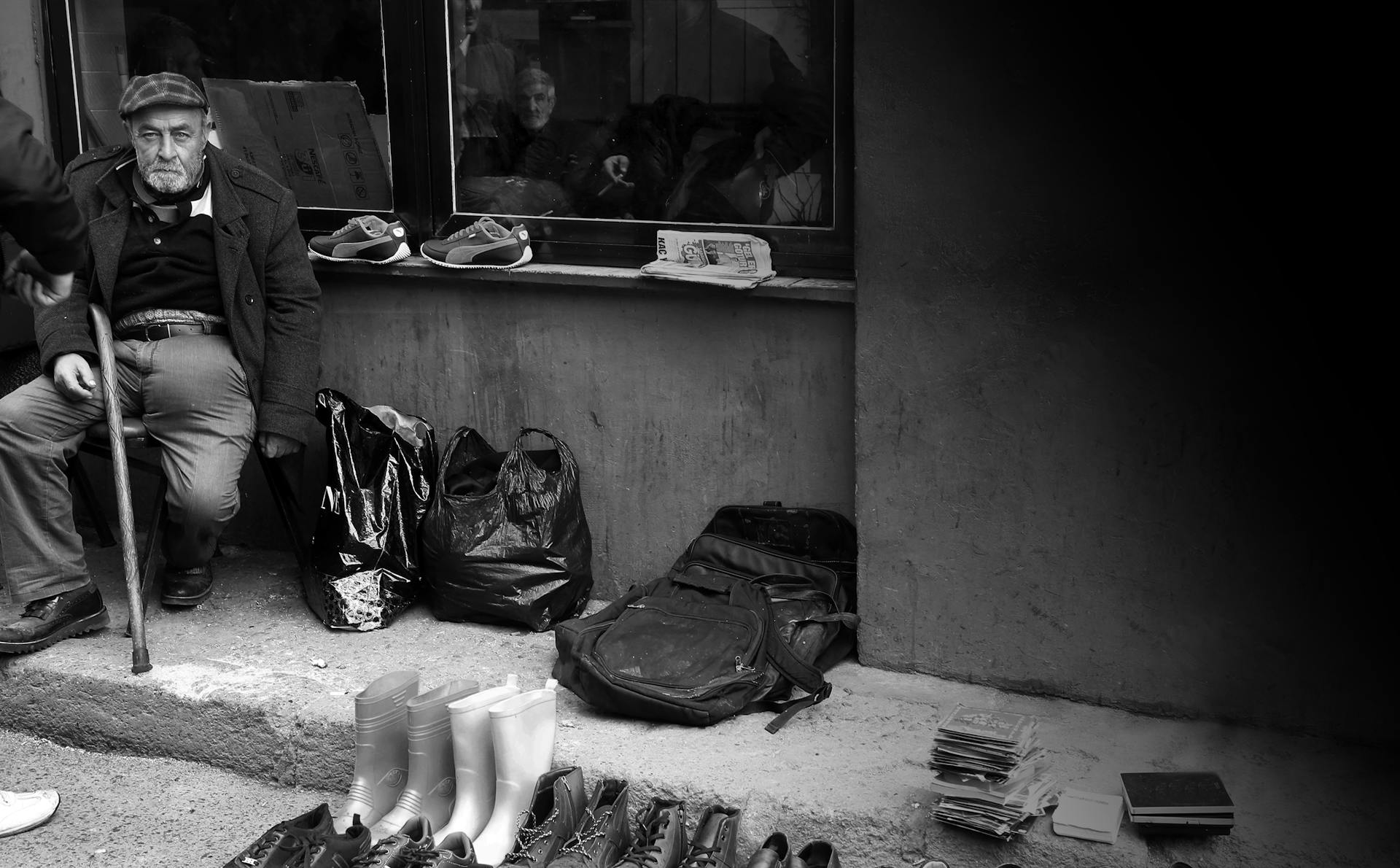 Black and white photo of a street vendor selling shoes and bags, conveying a classic urban scene.