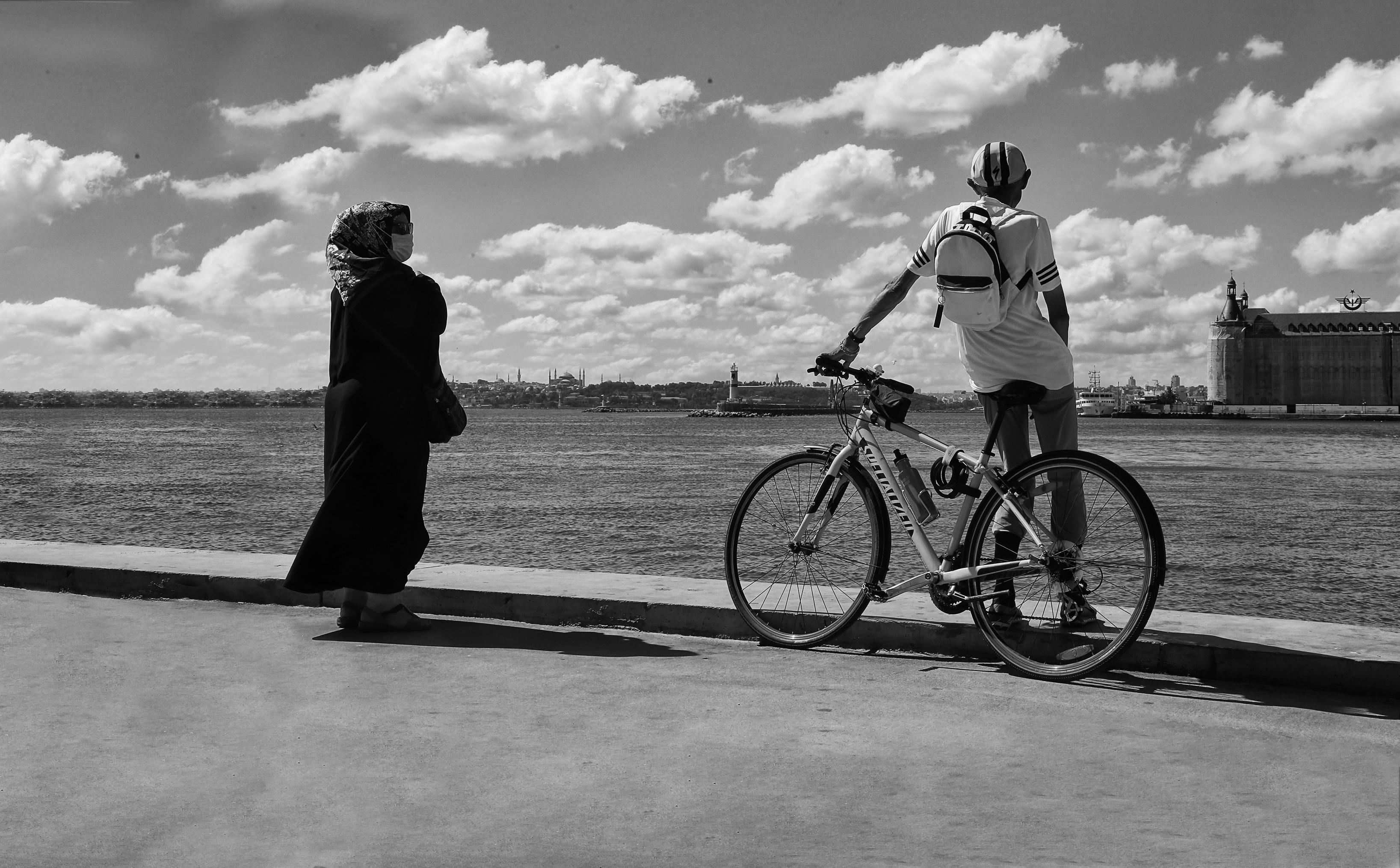 black and white photograph of a woman wearing a headscarf and a man leaning against a bike on a pier