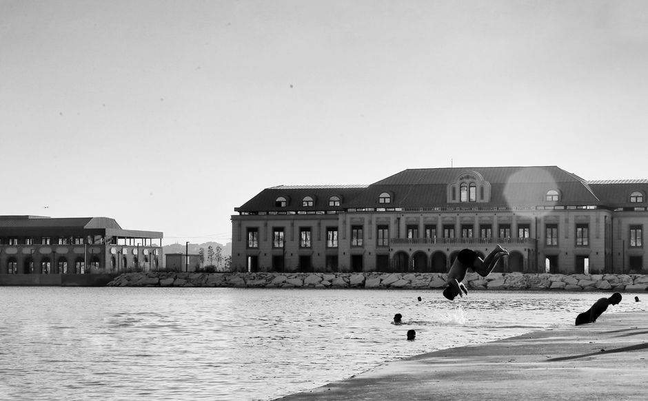 Foto en blanco y negro de jóvenes saltando a un río cerca de elegantes edificios frente al río.