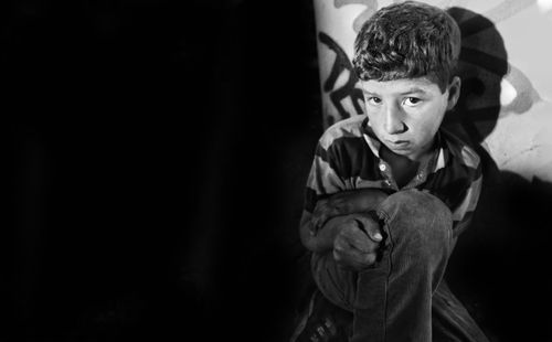 Free A contemplative young boy sits against a wall in a street setting. Stock Photo
