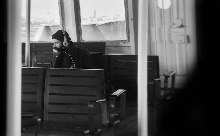 Black And White Photo Of Man Wearing Headphones Sitting In Empty Boat