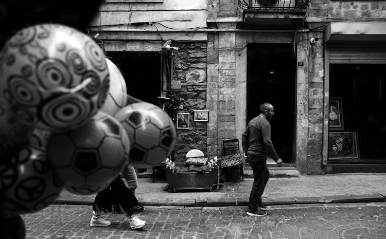 People Walking In An Alley By The Traditional Buildings And Person Selling Balloons 