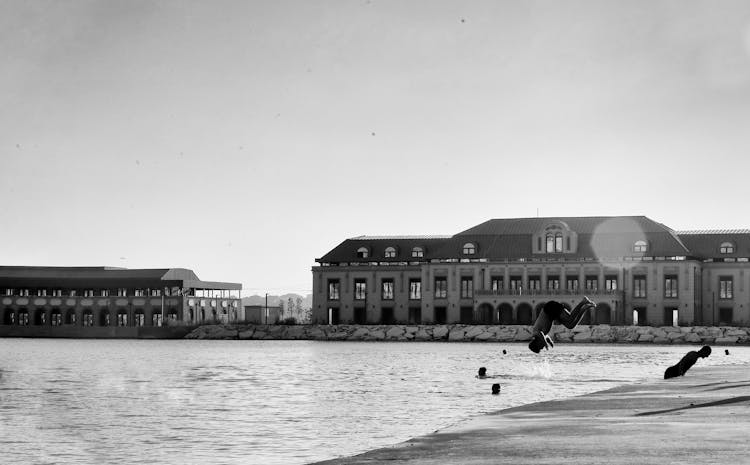 Black And White Photograph Of A Waterfront And A Man Jumping Into Water