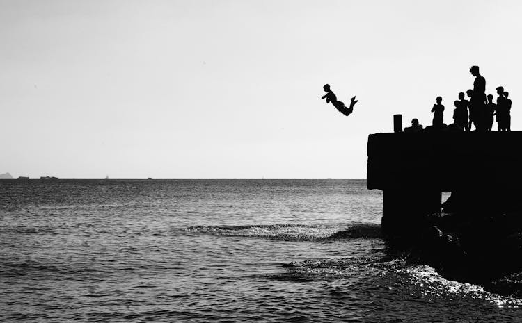 Silhouette Of A Man Jumping From The Pier Into The Sea 