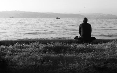 A Grayscale of a Man Sitting and Looking at the Sea