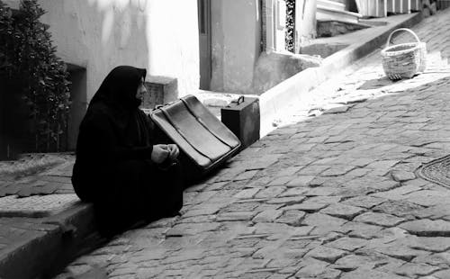A Grayscale of a Woman in a Hijab Sitting on a Curb