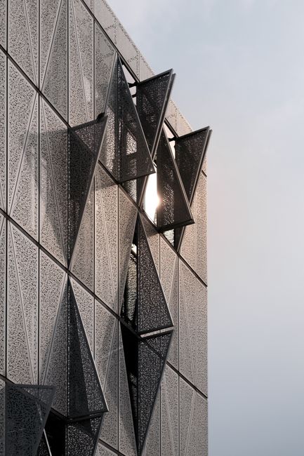 Triangular geometric facade with intricate patterns reflecting sunlight, showcasing modern architecture.