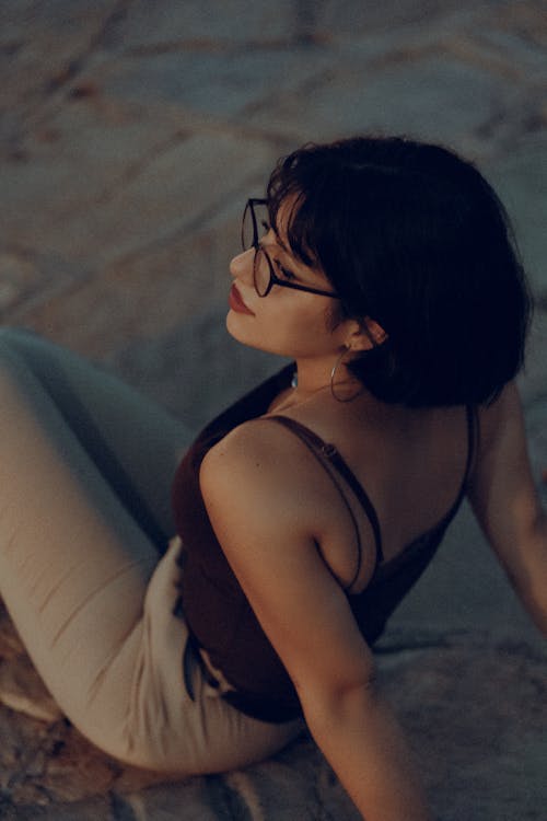 Woman in Black Spaghetti Strap Top and Beige Pants Sitting on the Ground