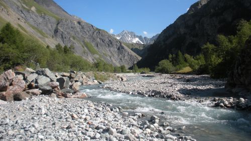Free A picturesque mountain stream flows through a rocky valley under a clear blue sky. Stock Photo