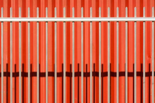 Free Modern metal fence casts shadows on a vibrant red wall, highlighting geometric patterns. Stock Photo