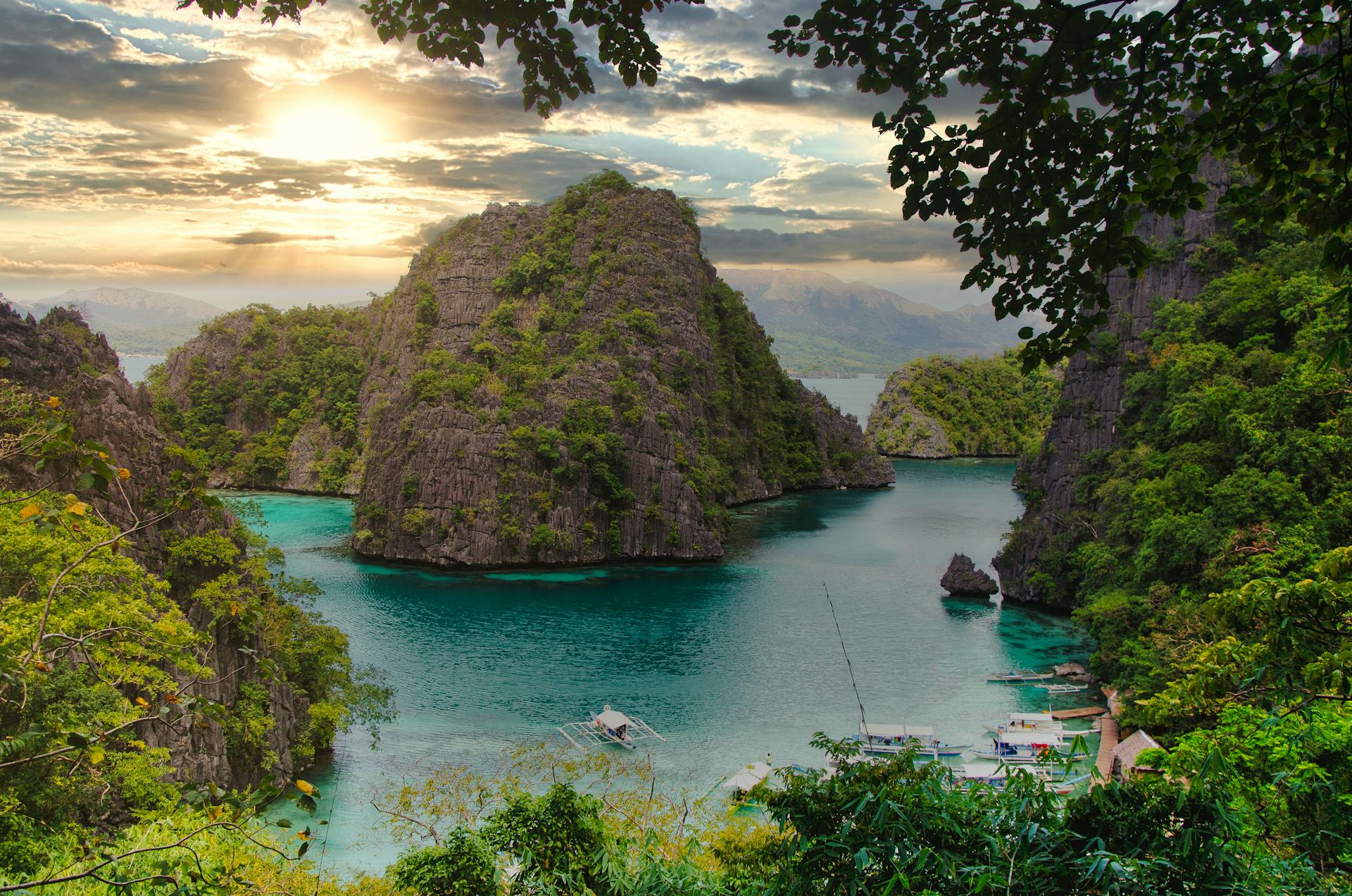 Scenic aerial view of Coron Bay, Philippines at sunset, with towering limestone cliffs and turquoise waters.