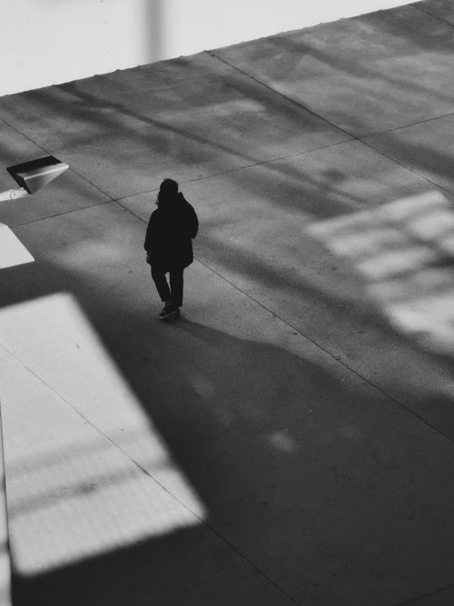 Free A solitary figure walks against harsh urban shadows in a striking black and white composition. Stock Photo