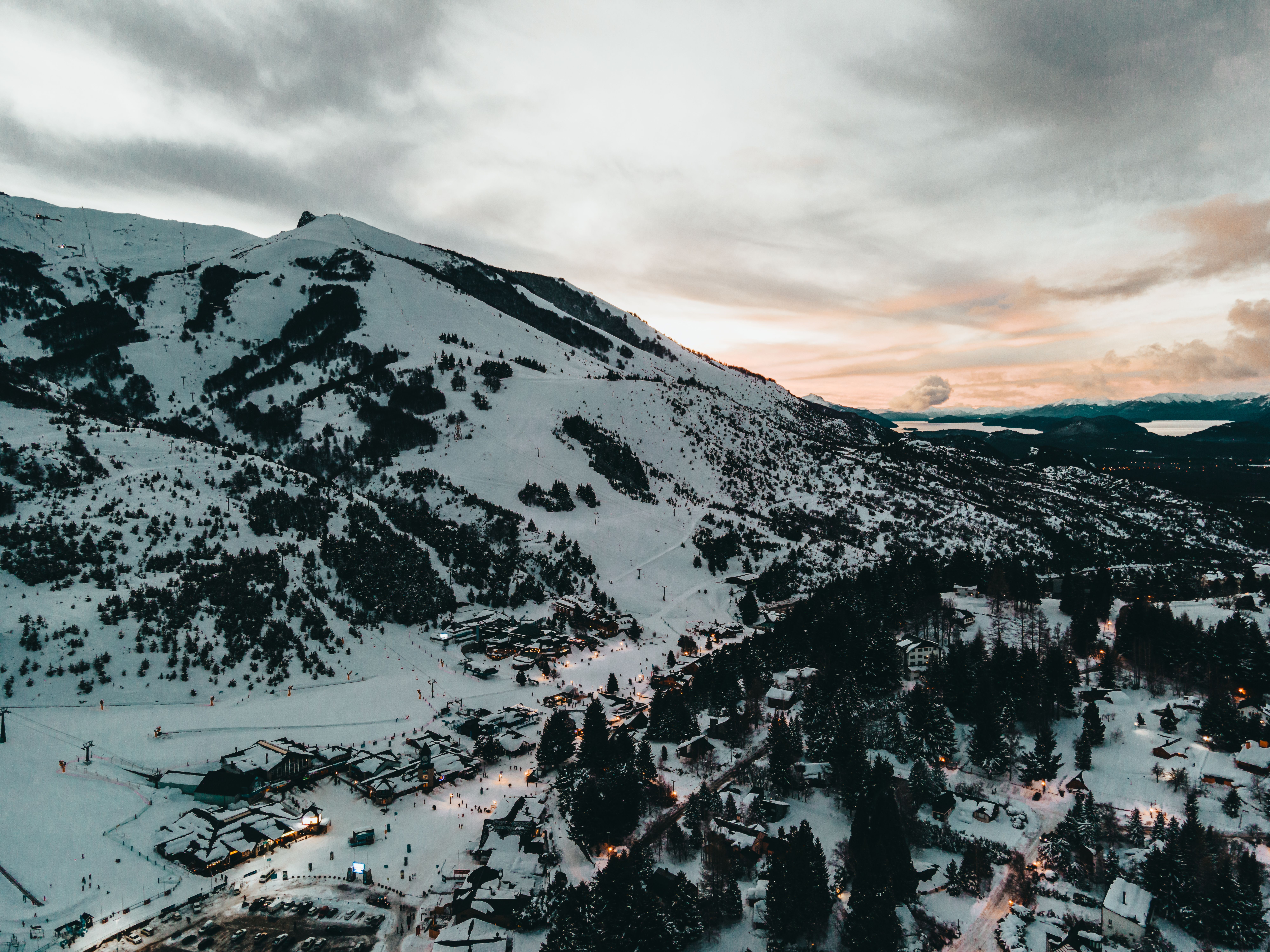 Aerial view of Villa Cerro Catedral, Argentina, blanketed in snow at dusk, with mountain peaks rising behind the village.