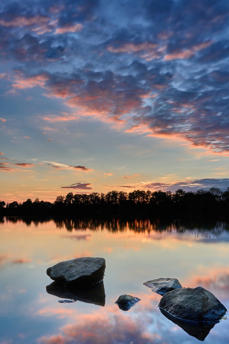 Body Of Water With Rocks Near Trees During Sunset