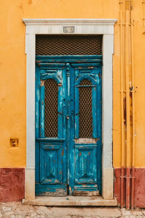 Free A rustic blue wooden door set against a vibrant yellow wall. Stock Photo