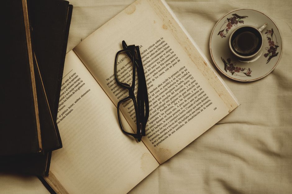 A warm atmosphere of relaxation featuring an open book, eyeglasses, and a cup of coffee on a saucer.