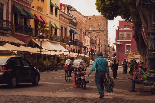 Free Colorful colonial street scene in Puebla de Zaragoza with people, vehicles, and colonial architecture. Stock Photo