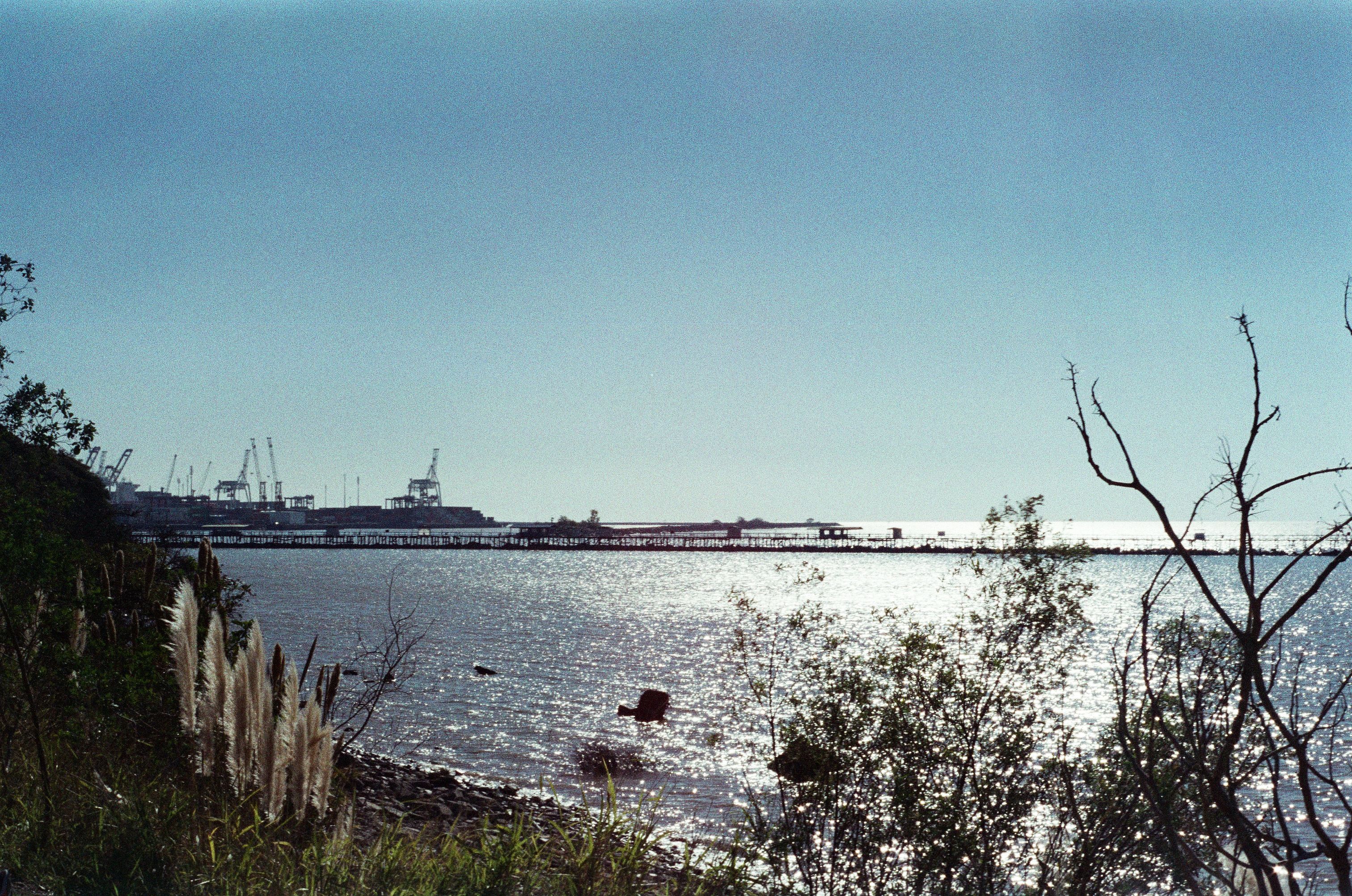 Peaceful coastal scene featuring a shimmering ocean and an industrial harbor in the distance.