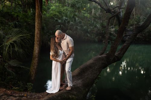 Free Pregnant couple shares a tender moment on a tree near a forest lake. Stock Photo
