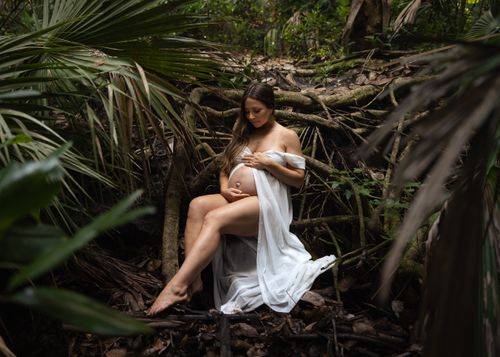 Free Pregnant woman in white dress embraces nature sitting in a tranquil forest setting. Stock Photo