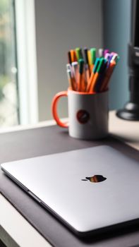 A modern laptop sits next to a mug filled with colorful pens on an office desk