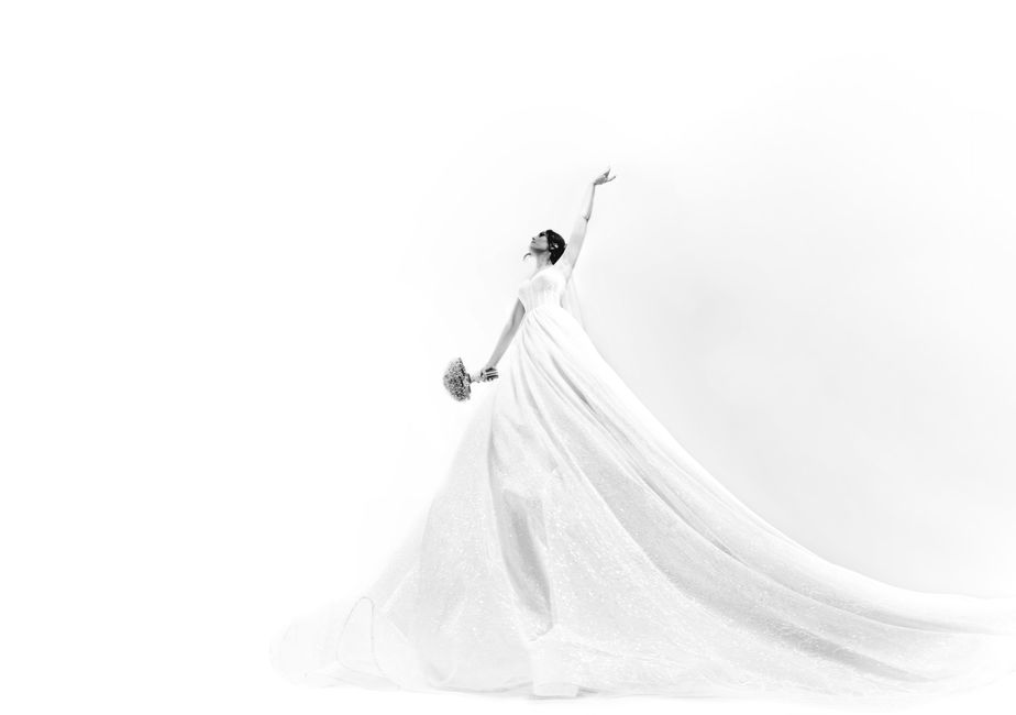 Graceful bride posing in a flowing gown against a white background.