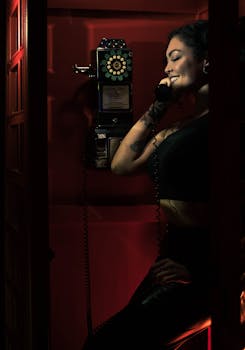 Woman smiling inside a vintage phone booth, making a call with a classic rotary phone.