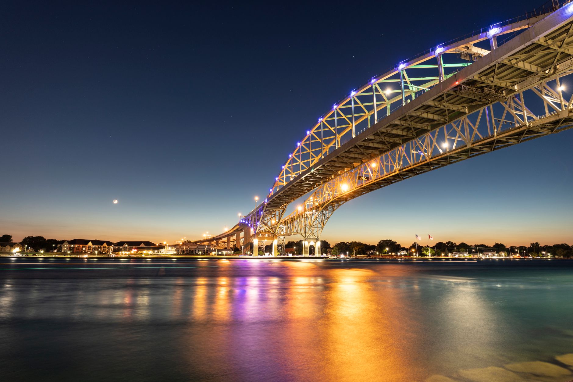 Stunning long exposure of the illuminated Blue Water Bridge at night over a calm river in Sarnia, Canada.