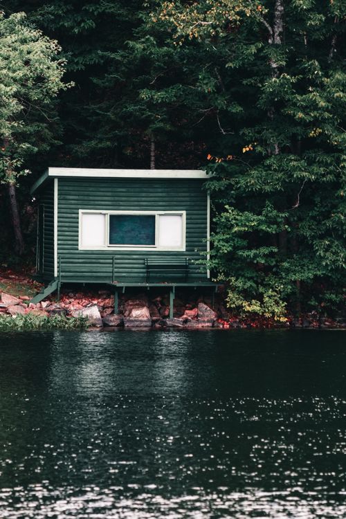 Free A serene green lakeside cottage nestled among the dense trees in Gatineau. Stock Photo