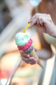 Close up of a woman's hand holding a two-scoop ice cream cone decorated with colorful sprinkles.
