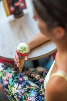 A woman holding a colorful ice cream cone at a cafe table, capturing a moment of enjoyment indoors.