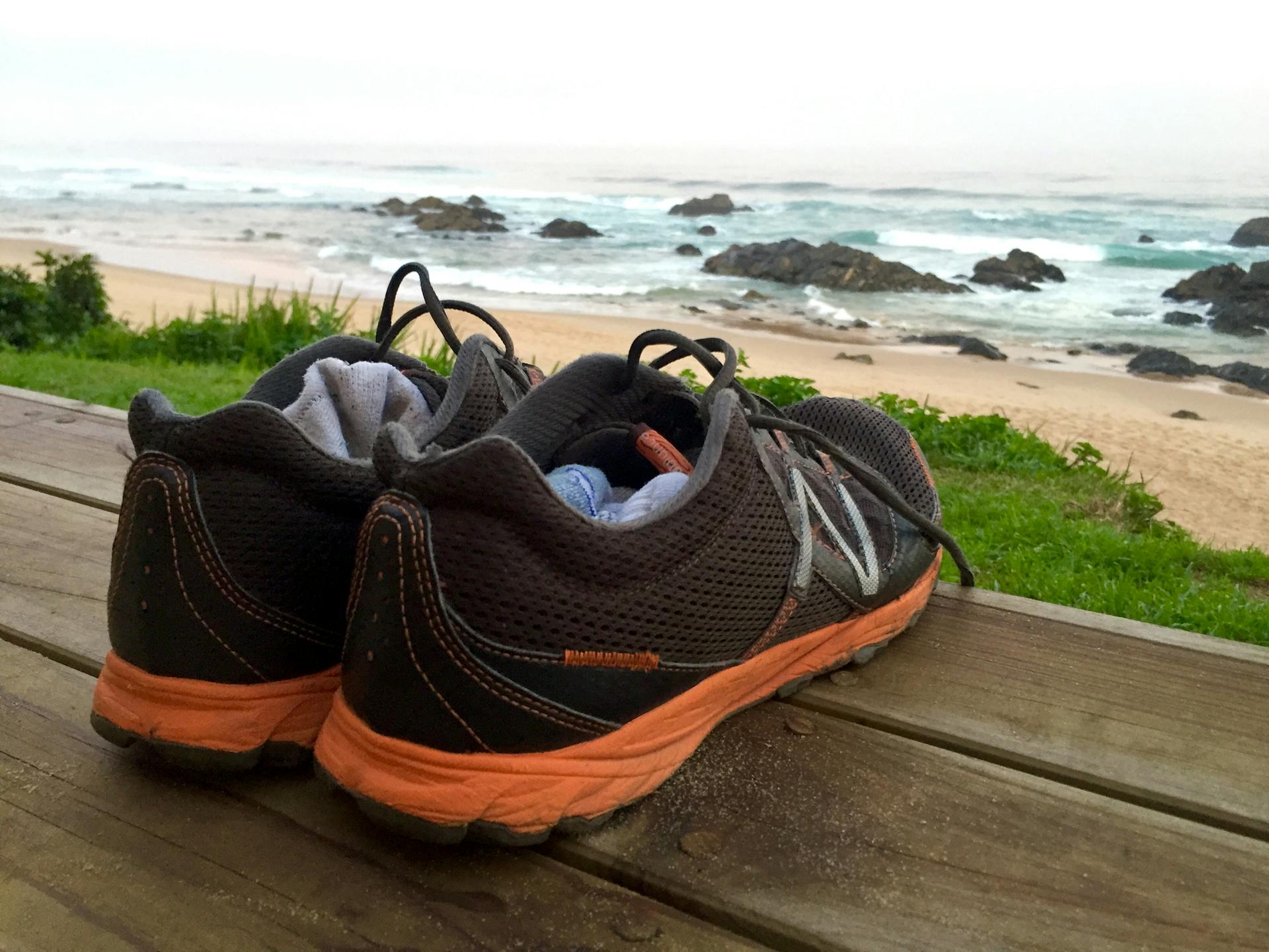 A pair of running shoes on a wooden deck overlooking the scenic Keurboomstrand beach in South Africa.