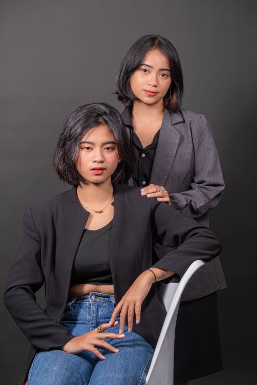 Free Studio portrait of two women in business blazers posing confidently against a dark backdrop. Stock Photo