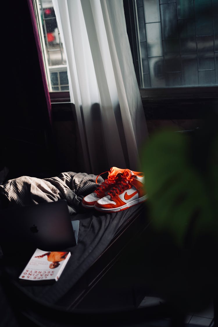 Shoes And Macbook On The Bed Beside The Window