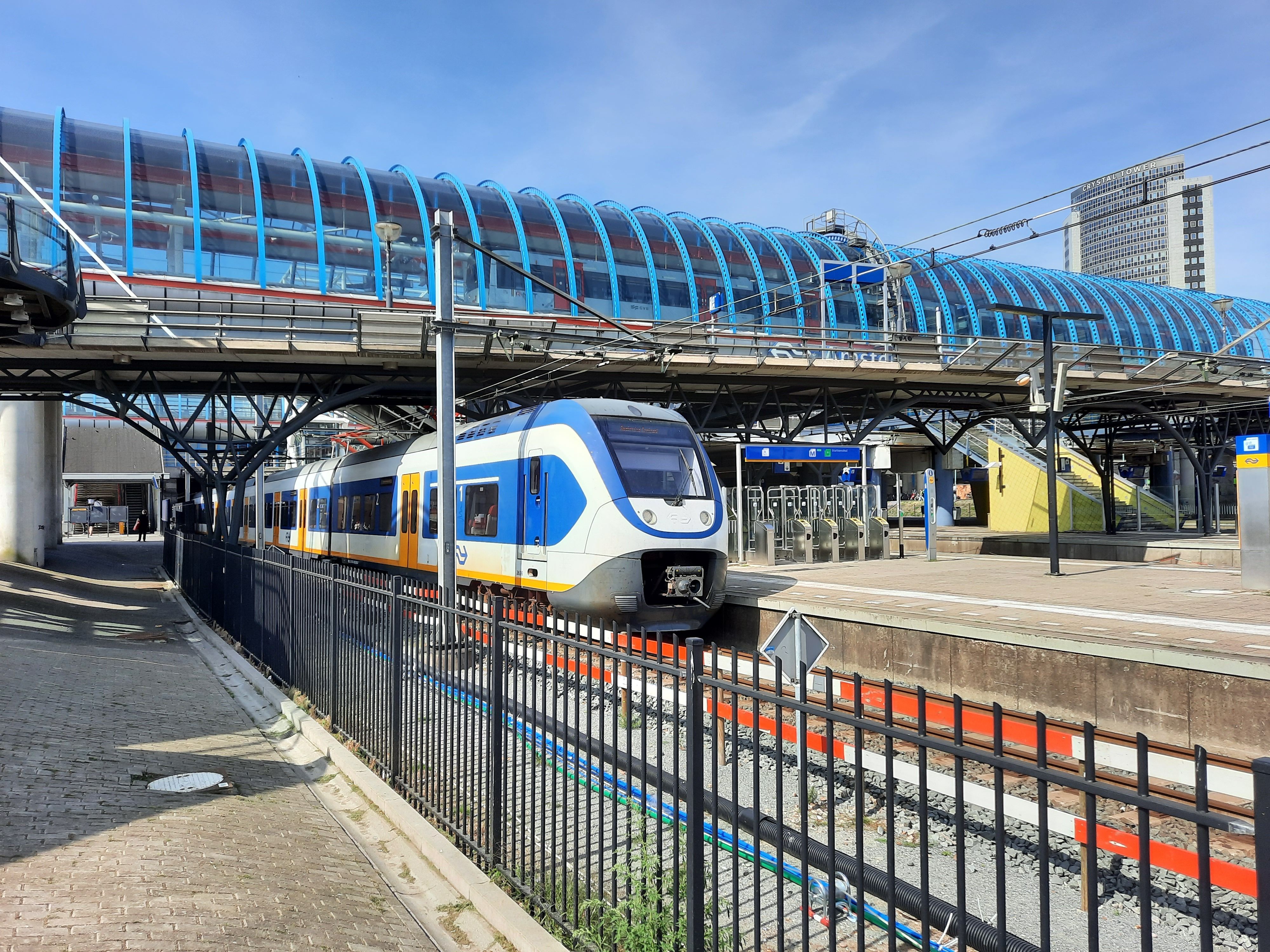 Een moderne trein rijdt station Amsterdam Sloterdijk binnen en toont hedendaagse architectuur en stedelijke infrastructuur.