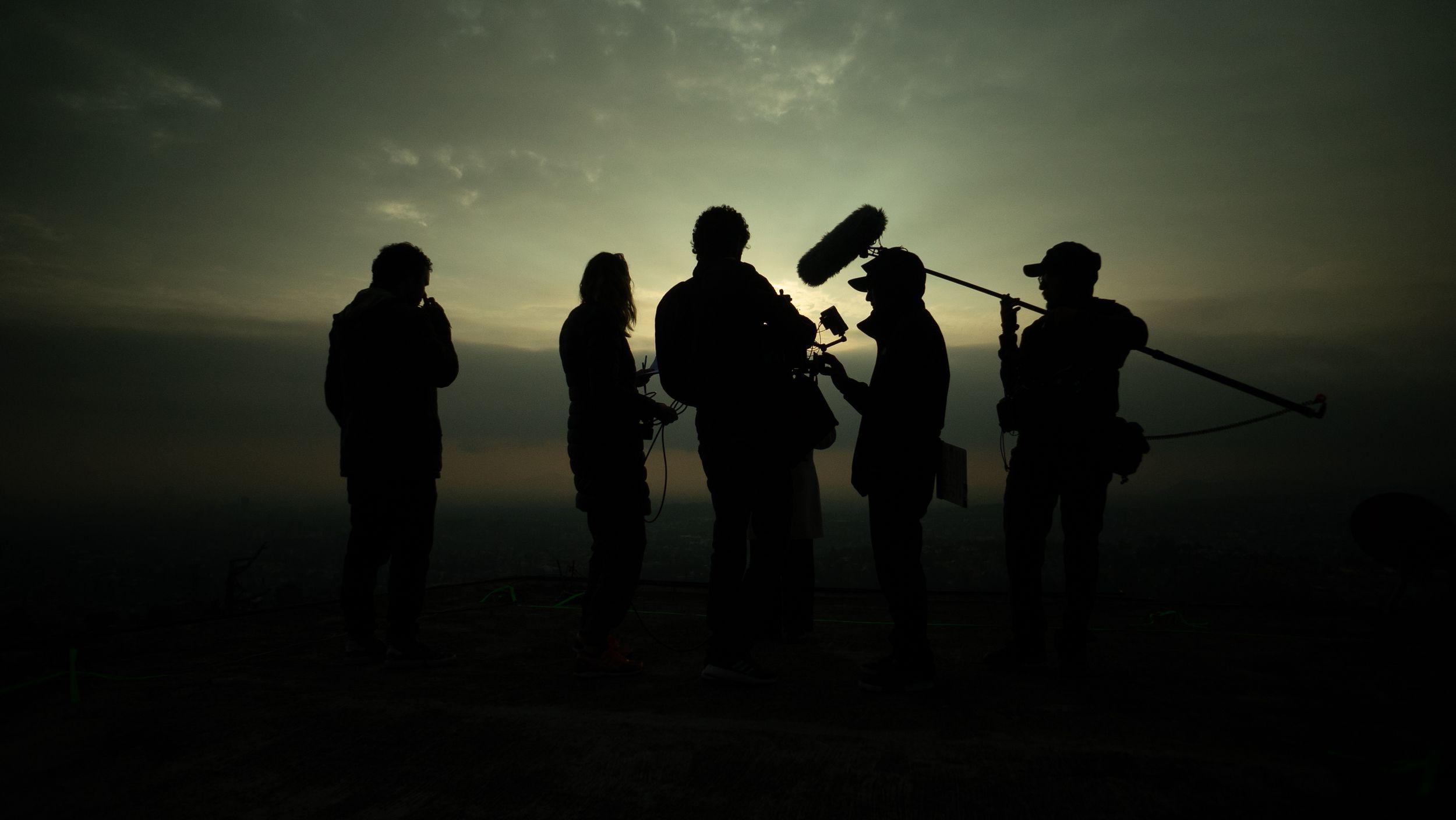 Silhouettes d’une équipe de tournage au coucher du soleil, lumière dorée et ciel dramatique