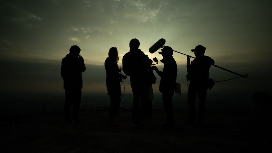 Film crew silhouettes shooting outdoors against a dramatic sunset