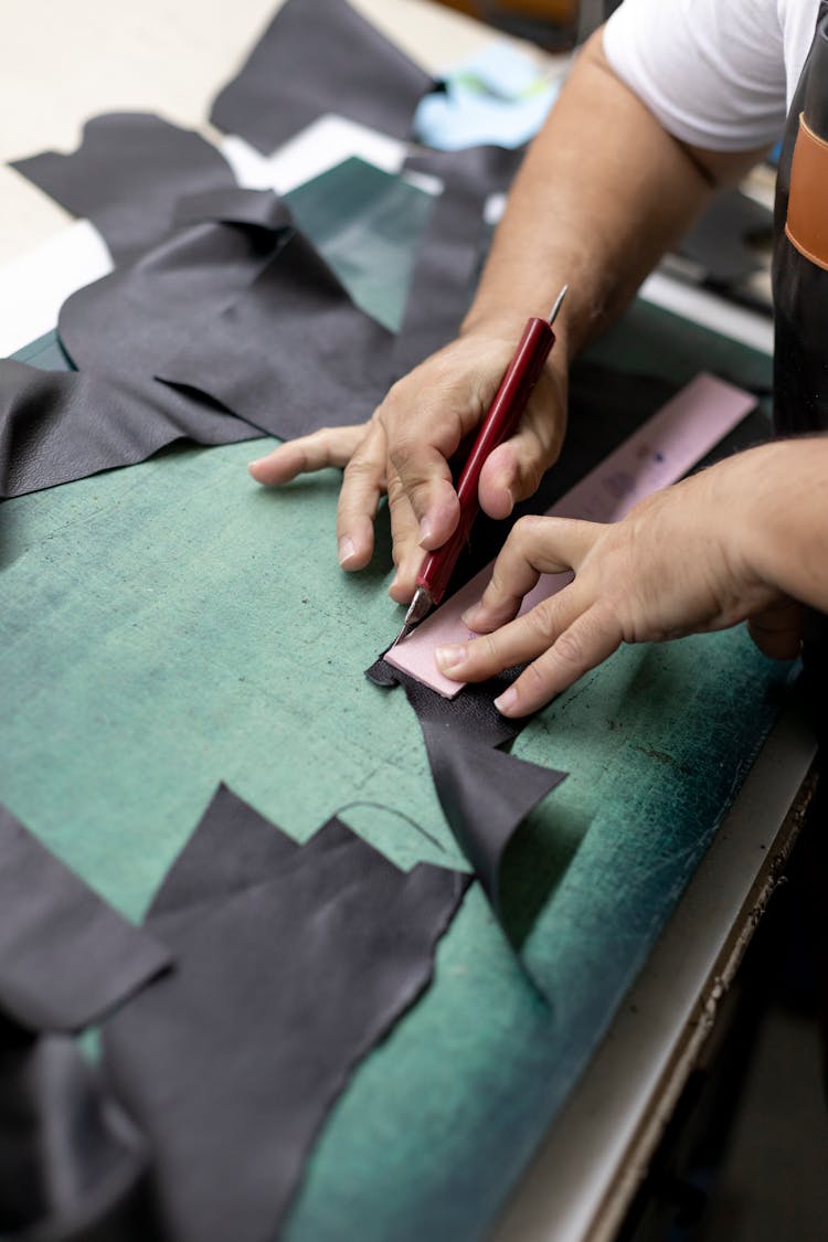 A Person Cutting The Fabric Using A Ruler And Cutter