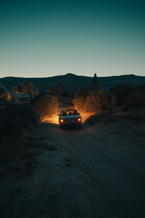 Free A car drives through a dark countryside path with headlights illuminating the way beneath a serene sky. Stock Photo