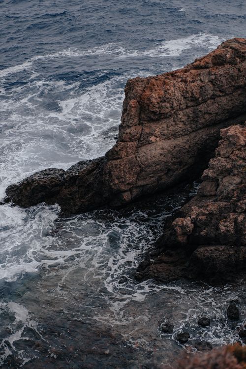 Free Powerful ocean waves crash into rugged rock formations along the shore creating a dramatic seascape. Stock Photo