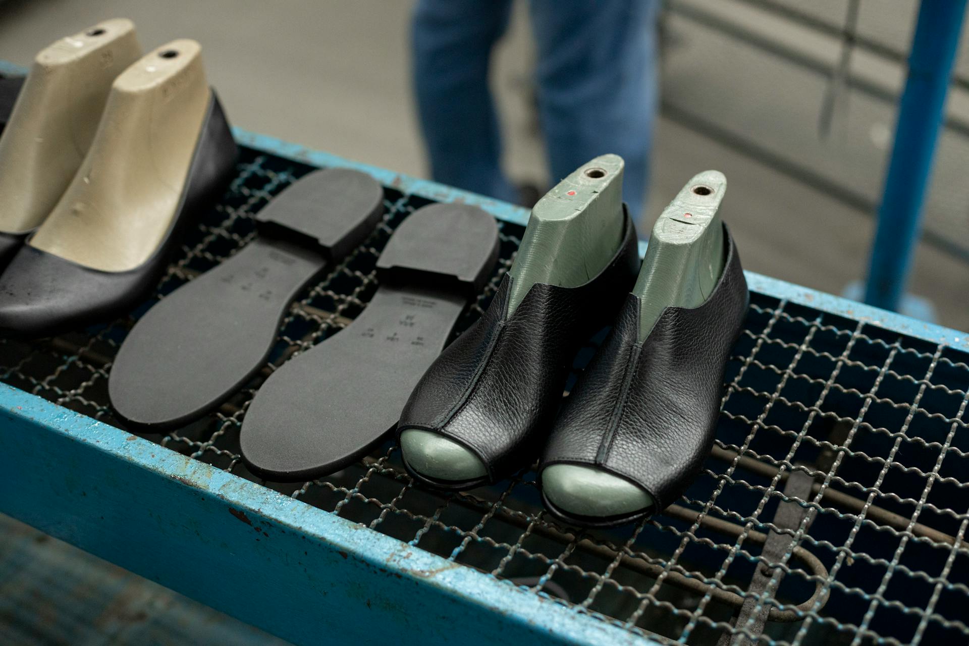 Detailed view of shoe making process with leather uppers and molds on work table.